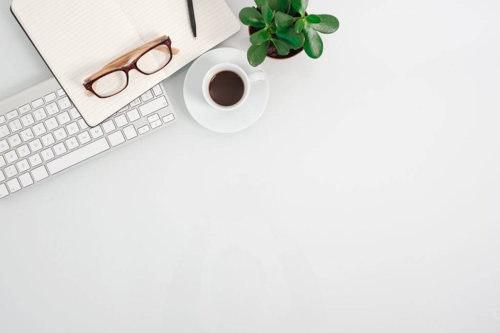 White office desk table with keyboard, plant, coffee and notepad on it